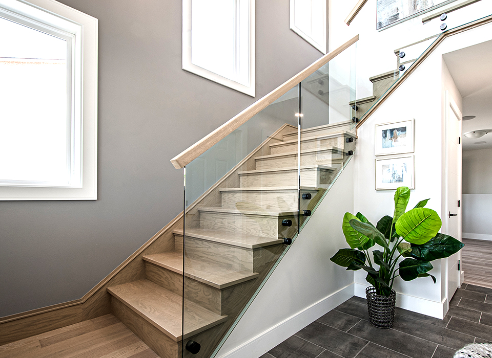 Bright residential staircase with a frameless glass railing system featuring black PVD-finished stainless steel glass standoffs, and a minimalist wood handrail, illustrating a modern glass railing stair design.